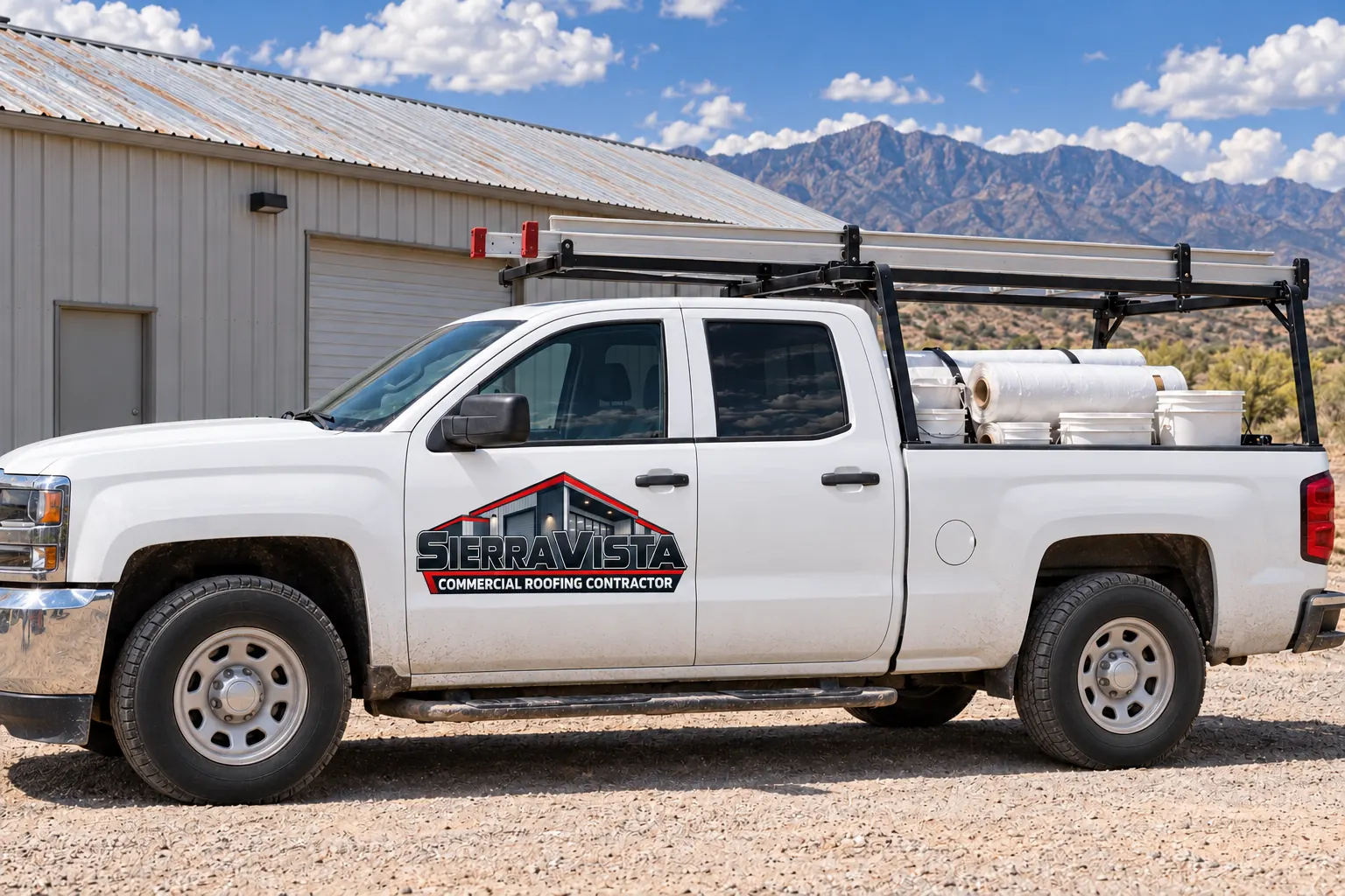 White work pickup loaded with roofing materials beside a metal-roofed light-industrial building